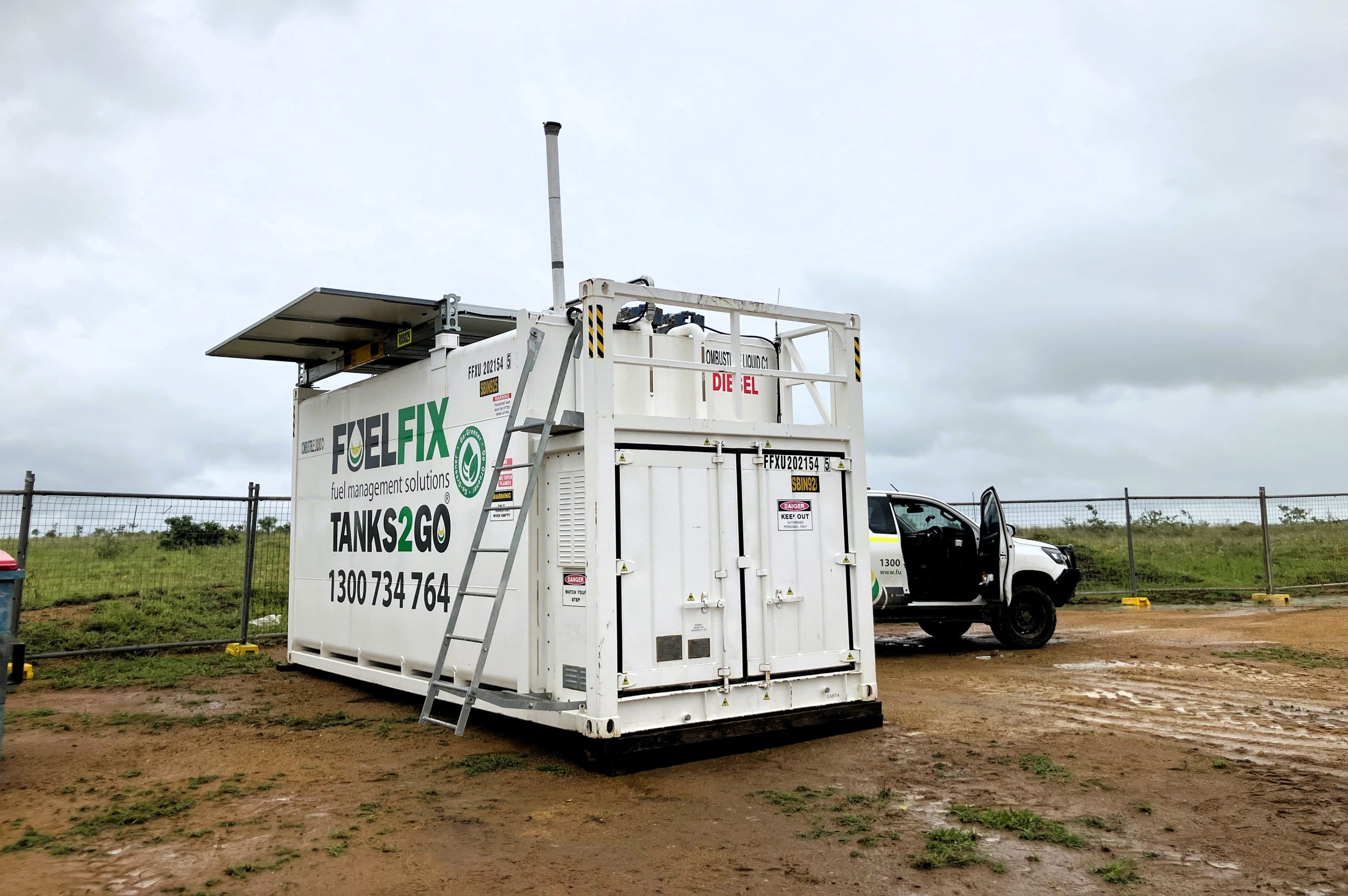 Fuelfix innovative solar-powered fuel tank system operating on a remote, muddy construction site for a wind farm project. The tank features solar panels and battery energy storage system, replacing diesel generators to power fuel dispensing for service vehicles, reducing emissions and operational costs.
